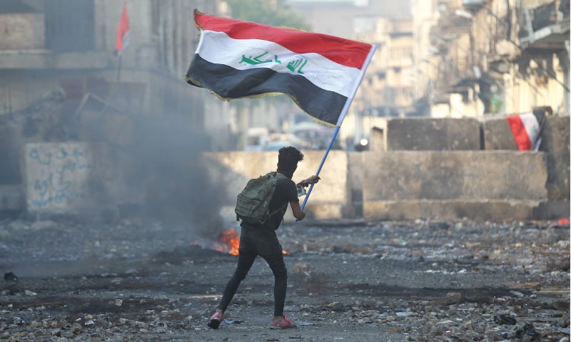 An Iraqi anti-government protester waves a national flag close to a concrete barricade amidst clashes with security forces along Baghdad’s Rasheed Street on Friday.—AFP