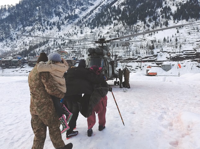 A SOLDIER escorts members of a stranded family to a helicopter in Neelum Valley. Search teams continued to pull out bodies on Thursday from homes destroyed by avalanches in Azad Kashmir.—AP