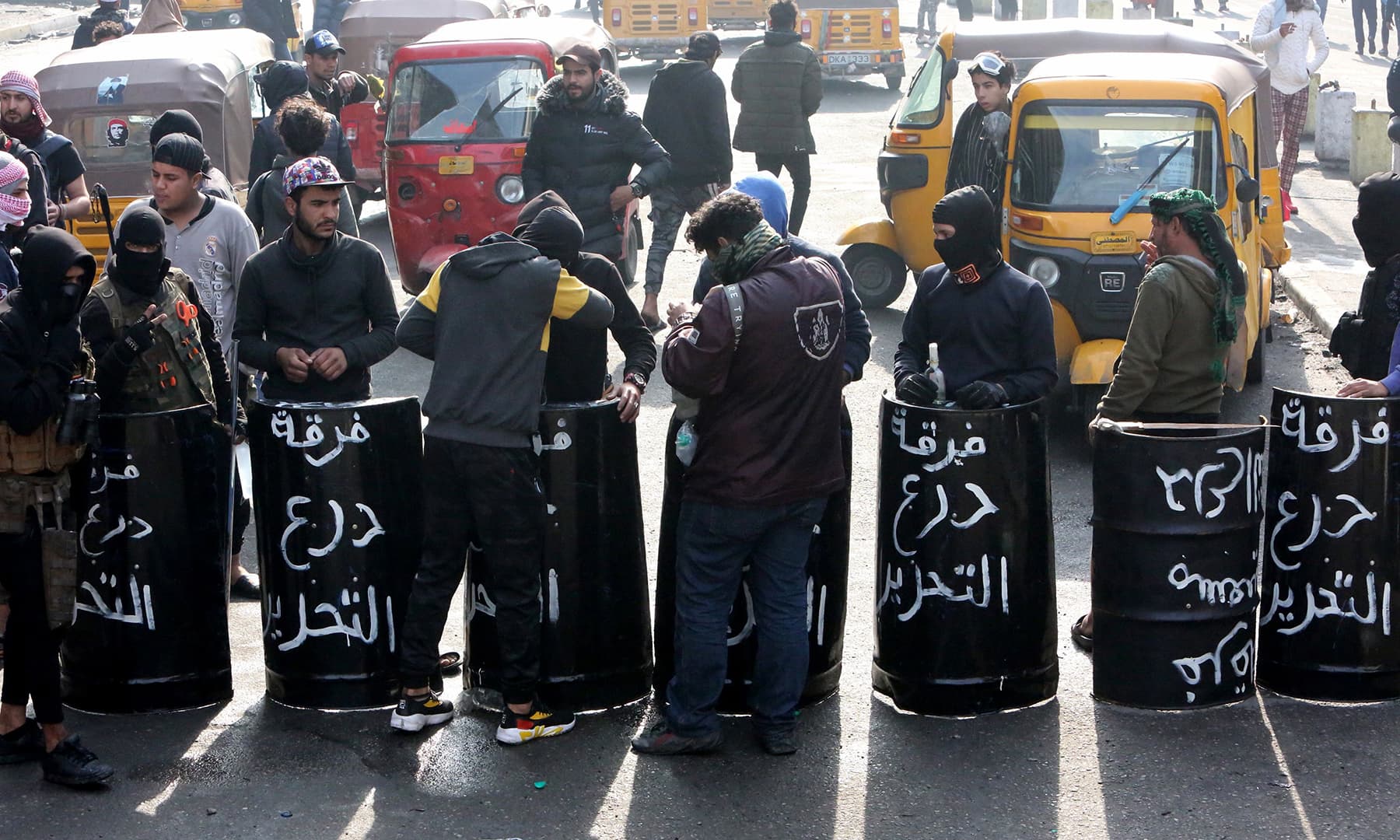 Iraqi anti-government protesters carry black shields made out of metal drums, on which they had painted the words "Tahrir Shield Squad.", as they gather at al-Sinek bridge in the capital Baghdad on Saturday. — AFP