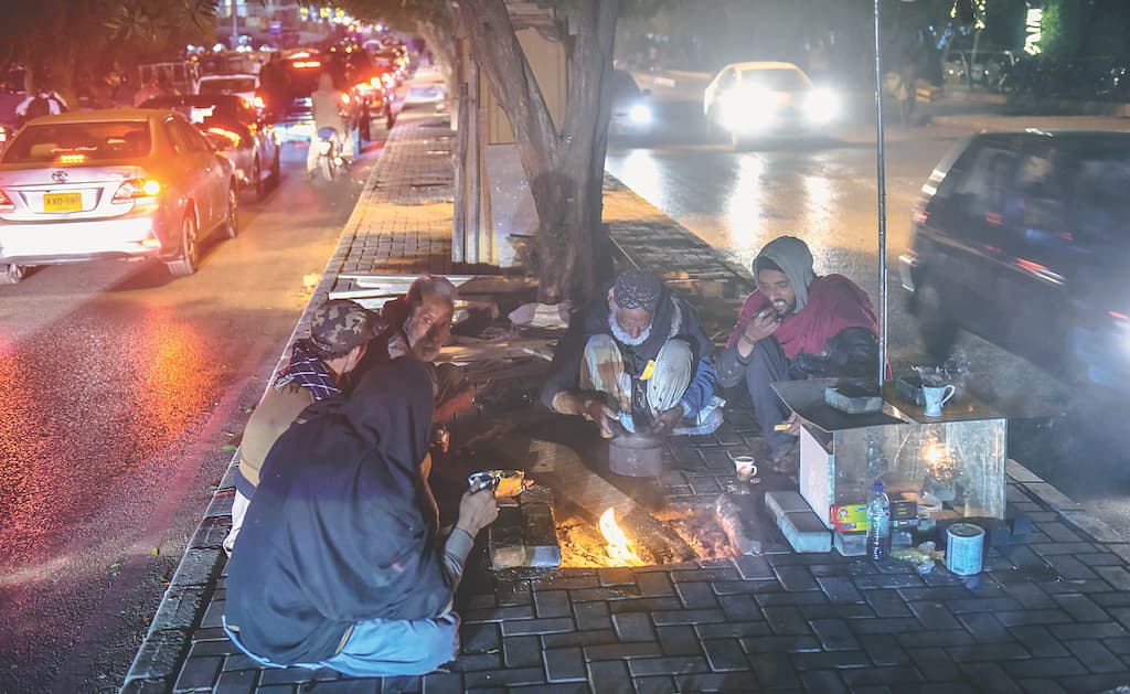 Men have dinner on a footpath by a busy road in Karachi | White Star