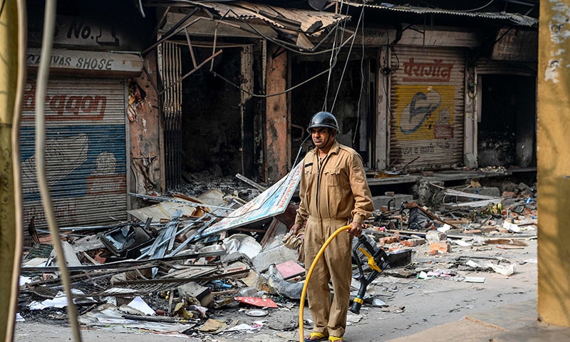 A firefighter stands holding a pipe on street near burnt-out premises following clashes between people supporting and opposing a contentious amendment to India's citizenship law in New Delhi on February 26. — AFP