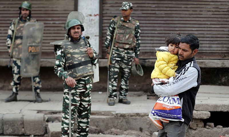 A man carrying a child walks past security forces in a riot affected area following clashes between people demonstrating for and against a new citizenship law in New Delhi, India on February 27. — Reuters