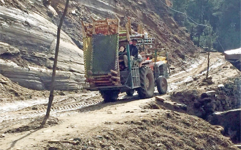 A tractor carrying charpoys moves on unpaved section of Mian Kallay road in Shangla. — Dawn