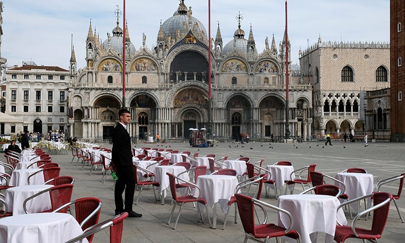 A waiter stands by empty tables outside a restaurant at St Mark's Square in Venice, Italy, March 9. — Reuters