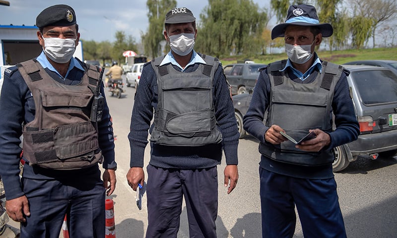 Policemen wearing facemasks stand at the capital entry checkpoint in Islamabad on March 14. — AFP