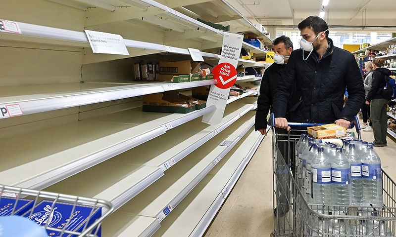 Shoppers wearing masks are faced with partially empty shelves at a supermarket in London on March 14, 2020, as consumers worry about product shortages, leading to the stockpiling of household products due to the outbreak of the novel coronavirus. Faced with supermarkets being emptied and online shopping overrun due to the COVID-19 pandemic, UK retailers are appealing to consumers to come to their senses and ensure that the country will not run out of food. — AFP