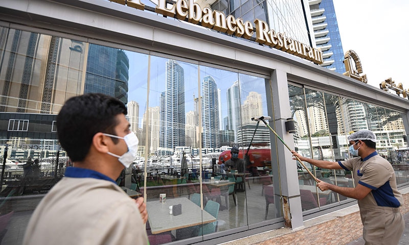Labourers, wearing protective face masks, disinfect the front of a restaurant in Dubai's marina on March 16, 2020. &mdash; AFP