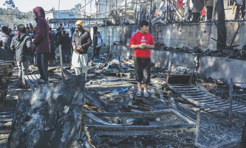 LESBOS: Migrants stand on a burned container home in a refugee camp on the Greek island of Lesbos on Monday.—AP