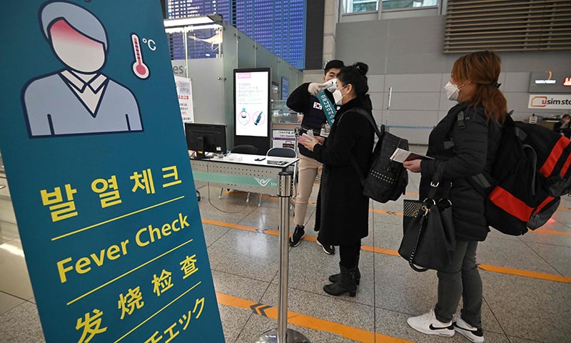 A member of the South Korean military support team (L) checks the body temperature of a passenger at a gate in the departure hall at Incheon international airport on March 17. &mdash; AFP