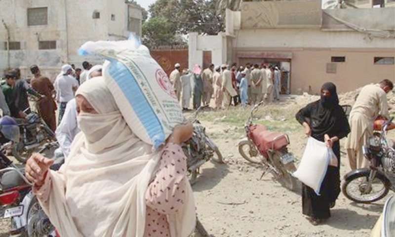 TWO women take away bags of flour while other people queue up for the essential commodity at a Korangi mill on Sunday. —Online