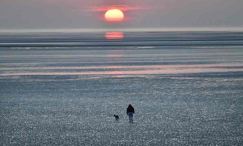 A woman walks her dogs as they take their exercise along the beach at sunset in Leasowe, north west England on March 25, after Britain's government ordered a lockdown to slow the spread of the novel coronavirus. Britain was under lockdown, its population joining around 1.7 billion people around the globe ordered to stay indoors to curb the "accelerating" spread of the coronavirus. &mdash; AFP