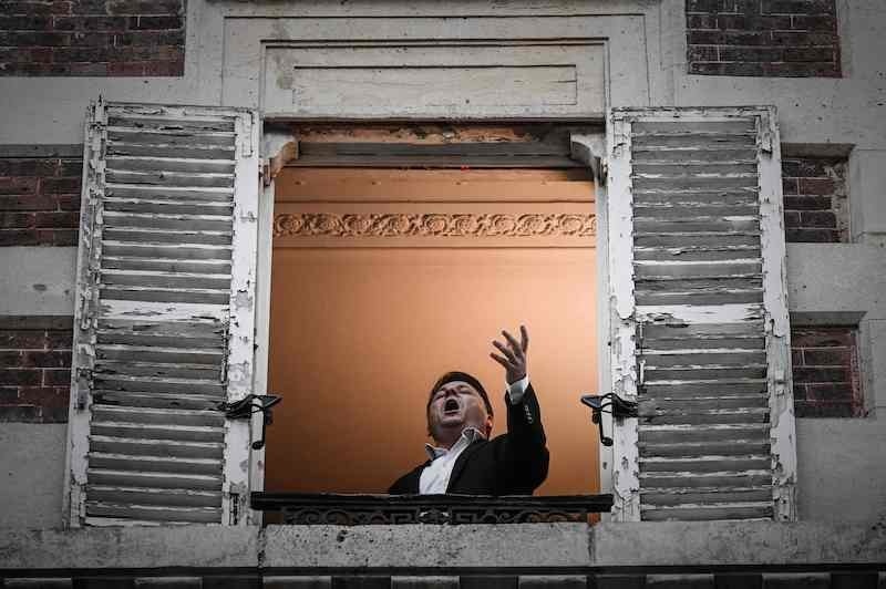 An opera tenor singer performs the song O sole mio from his window in Paris on March 26, 2020, on the evening of the tenth day of a strict lockdown in France aimed at curbing the spread of Covid-19, caused by the novel coronavirus. — AFP