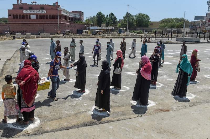 People stand in designated areas marked on the ground to maintain social distancing as they receive free food from volunteers of Chhipa Welfare Association during a government-imposed lockdown as a preventive measure against the coronavirus in Karachi on March 27, 2020. — AFP