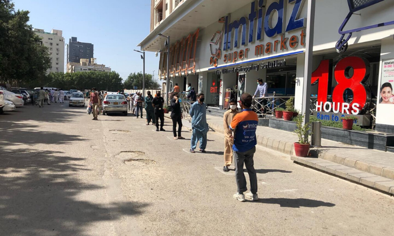 People practise social distancing while standing in queues outside a supermarket in Karachi for their turns to shop. &mdash;Dawn.com