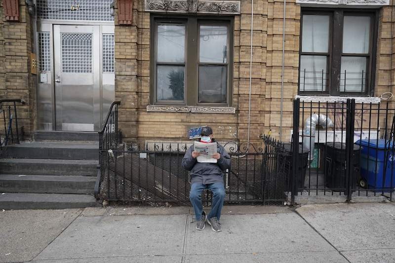 A man wearing a surgical mask reads the newspaper on the sidewalk in the Bushwick section of the Borough of Brooklyn on March 31, 2020, in New York. A military hospital ship arrived in New York on March 30 as America's coronavirus epi-centre prepares to fight the peak of the pandemic that has killed over 2,500 people across the US. The navy's 1,000-bed USNS Comfort entered a Manhattan pier around 10:45am. It will treat non-virus-related patients, helping to ease the burden of hospitals overwhelmed by the crisis. — AFP