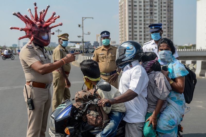 Police inspector Rajesh Babu (C) wearing coronavirus-themed helmet speaks to a family on a motorbike at a checkpoint during a government-imposed nationwide lockdown as a preventive measure against the coronavirus in Chennai on March 28, 2020. One minute they're dancing in the street in comical coronavirus helmets, the next they're seen beating people for flouting a nationwide lockdown &mdash; Indian police have played good cop, bad cop in a bid to halt the spread of coronavirus. The streets of India's cities have been largely deserted for more than a week of the government's 21-day lockdown &mdash; no mean feat in a country of 1.3 billion people famed for their flexible attitude towards authority. &mdash; AFP