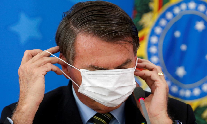 Brazil's Jair Bolsonaro adjusts his protective face mask during a news conference to announce measures to curb the spread of Covid-19 in Brasilia, Brazil March 18. &mdash; Reuters