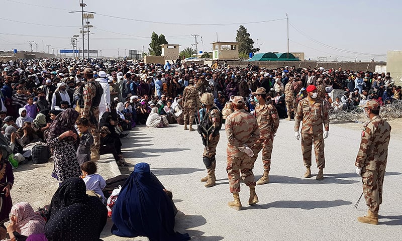 Afghan nationals wait to cross the border as security personnel wearing facemasks stand beside them at Chaman on Tuesday. — AFP