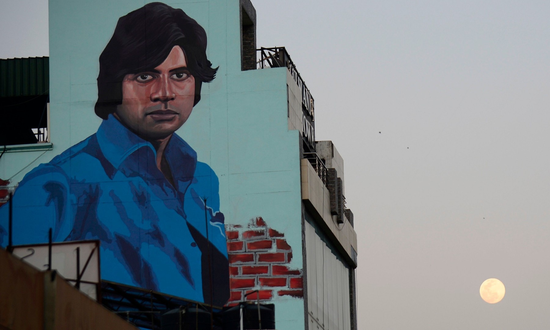 The full moon is seen next to a mural depicting Bollywood actor Amitabh Bachchan in India. &mdash; AFP