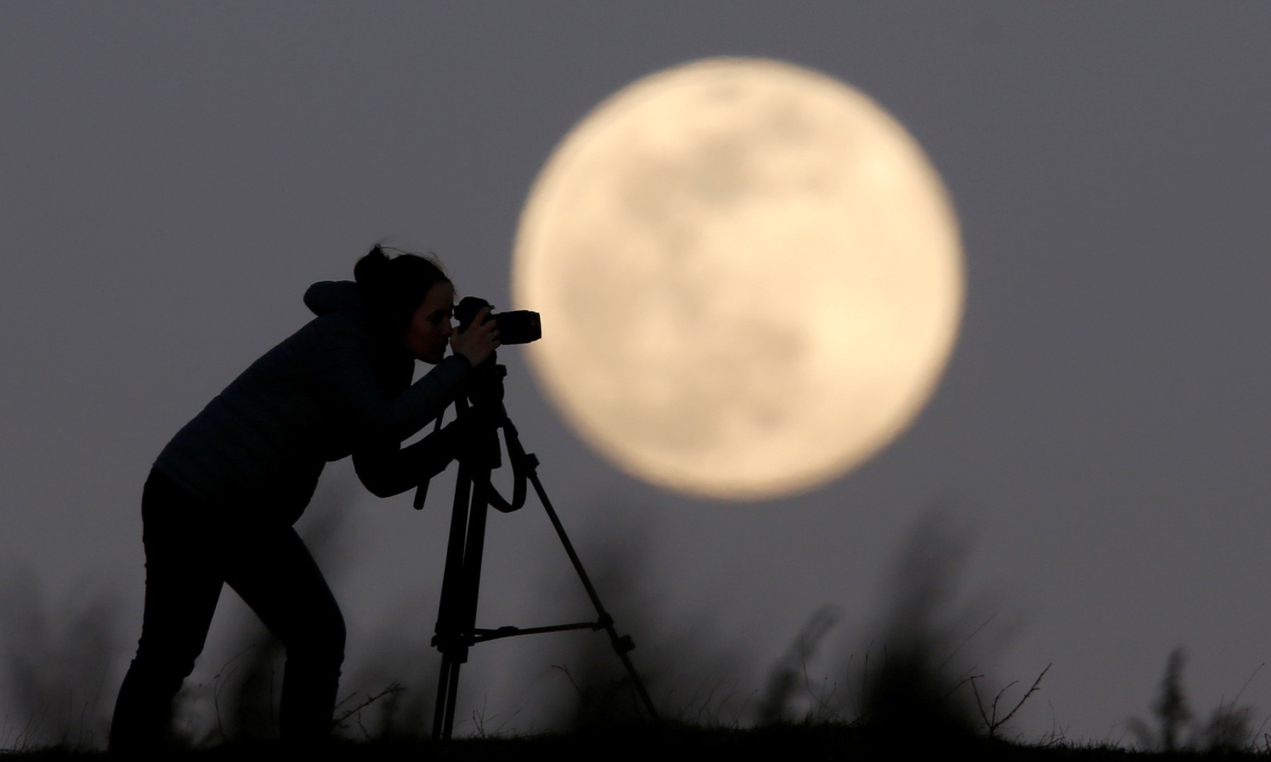A woman photographs the Pink Supermoon over mountain Smetov, Bosnia. &mdash; Reuters.