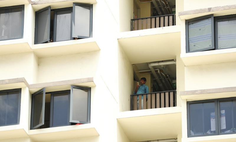 A foreign worker talks on the phone outside his room at the WestLite Toh Guan dormitory after it was declared an isolation area. &mdash; AP