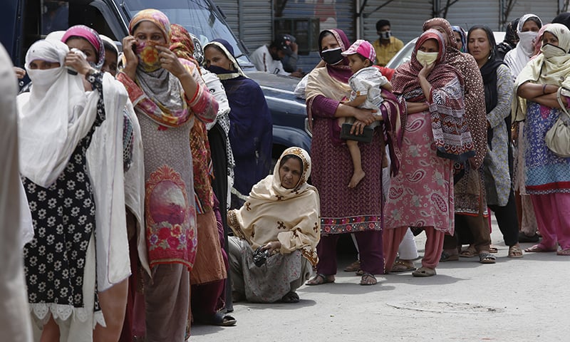 Women wait their turn to receive cash under the governmental programme in Lahore. &mdash; AP