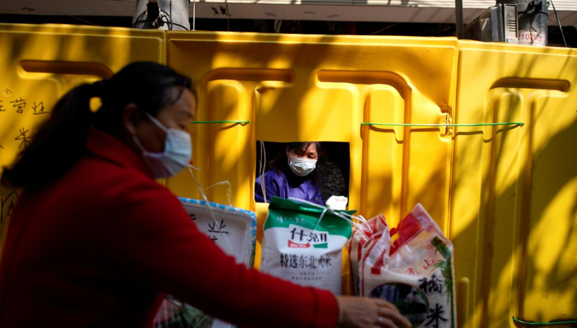 A resident (R) wearing a face mask buys food from a grocery stall through a small window opened on barriers which have been built to separate residential buildings from a street in Wuhan, capital of Hubei province and China's epicentre of Covid-19 outbreak, April 12. &mdash; Reuters