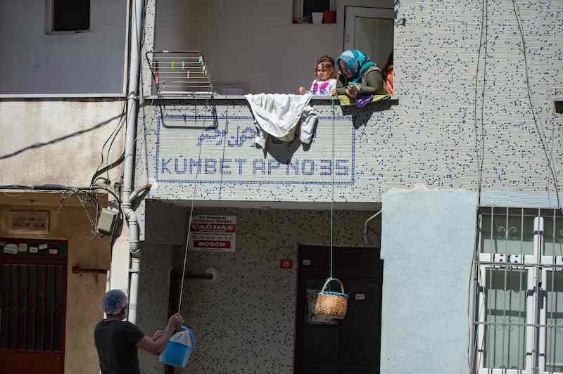 A baker puts bread in a basket hanged by a woman from her balcony as he delivers bread in his neighbourhood on April 11, 2020 in Istanbul, after Turkish authorities imposed a two-day curfew to prevent the spread of the coronavirus. — AFP