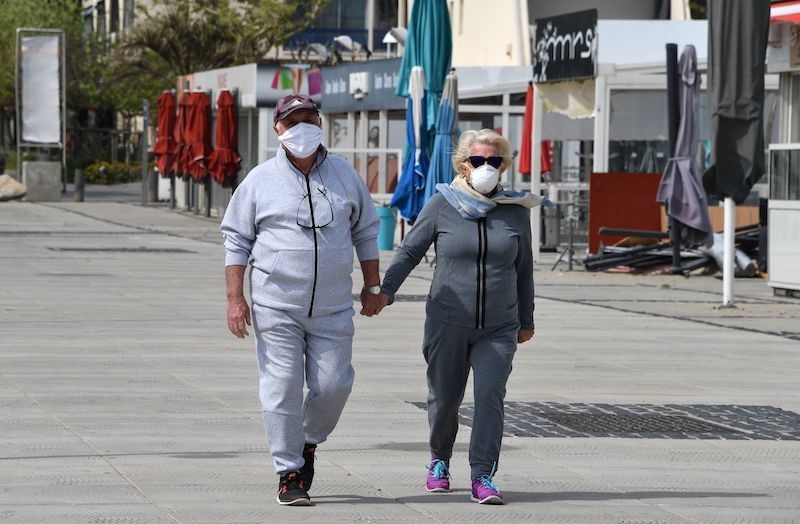 A couple wearing a protective mask and sportswear, walk past closed restaurants and shops by the seaside of La Grande-Motte, south of France, during Easter holidays on April 12, 2020, on the twenty-seventh day of a strict lockdown in France to curb the spread of the coronavirus. — AFP
