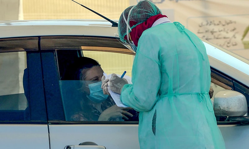 A medical staff member takes information from a resident sitting in a car for a coronavirus test at a drive-through screening and testing facility point in Karachi. — AFP/File