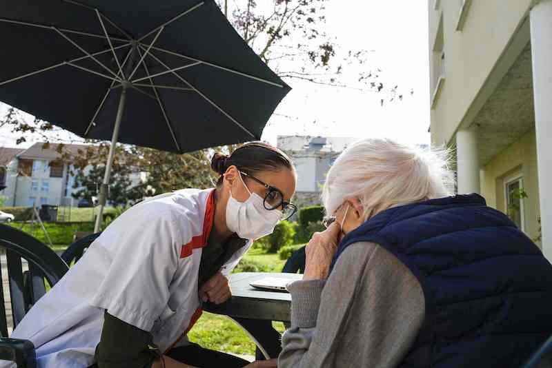A staff member of the Korian Vill'Alize EHPAD (Housing Establishment for Dependant Elderly People) in Thises, eastern France, speaks with a resident in the garden of the retirement home, on April 16, 2020 during the 31st day of a strict confinement in France aimed at curbing the Covid-19 disease. Due to the measures taken by the government to stop the spread of the virus, elderly people living the retirement home don't receive any visits from their relatives. — AFP