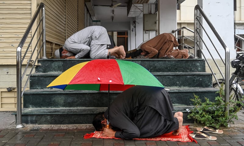 A worshipper holds an umbrella as he offers Friday prayers along with others outside a mosque in Islamabad. &mdash; AFP