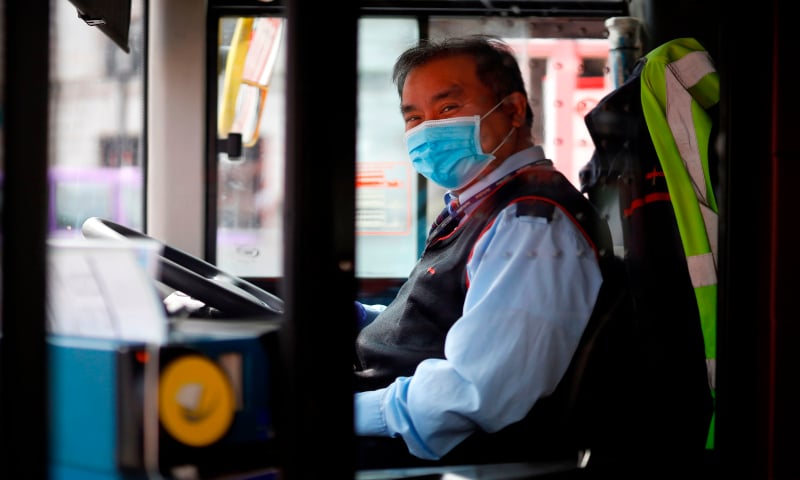 A bus driver wears a face mask as he sits in the driver's seat on a bus at Victoria Station, central London on April 17, 2020, during the Covid-19 pandemic. &mdash; AFP