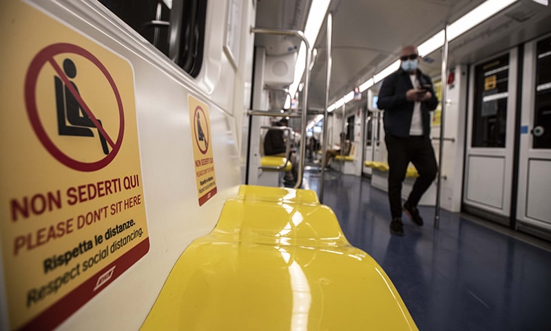 A man walks past signs reading 'please don't sit here, respect social distancing ', in a subway train in Milan, Italy, April 28. — AP