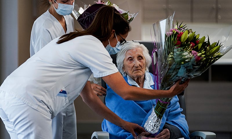 A medical worker offers flowers to Belgian 100-year-old patient Julia Dewilde as she leaves the Bois de l'Abbaye hospital in Seraing. &mdash; AFP