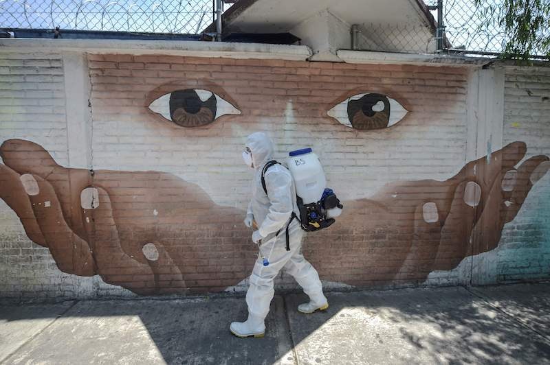 TOPSHOT - A cleaning worker wearing personal protective equipment (PPE) disinfects a street in Xochimilco, in Mexico City, on May 5, 2020, amid the new coronavirus pandemic. (Photo by PEDRO PARDO / AFP) &mdash; AFP or licensors