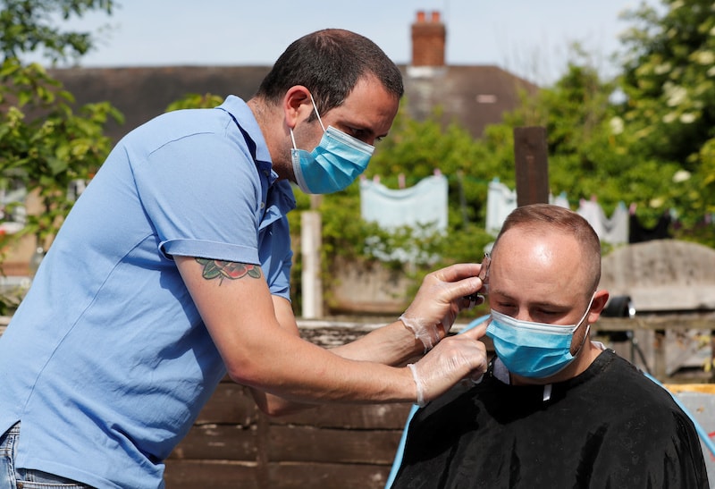 Hairdresser Pavlos cuts a man's hair in his garden as they both wear masks after his shop was shut due to government guidelines, following the outbreak of the coronavirus in Edmonton, Britain, on May 8, 2020. — Reuters