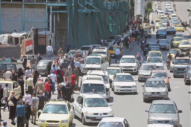 Pedestrians walk along a busy street in the Syrian capital on Sunday.—AFP