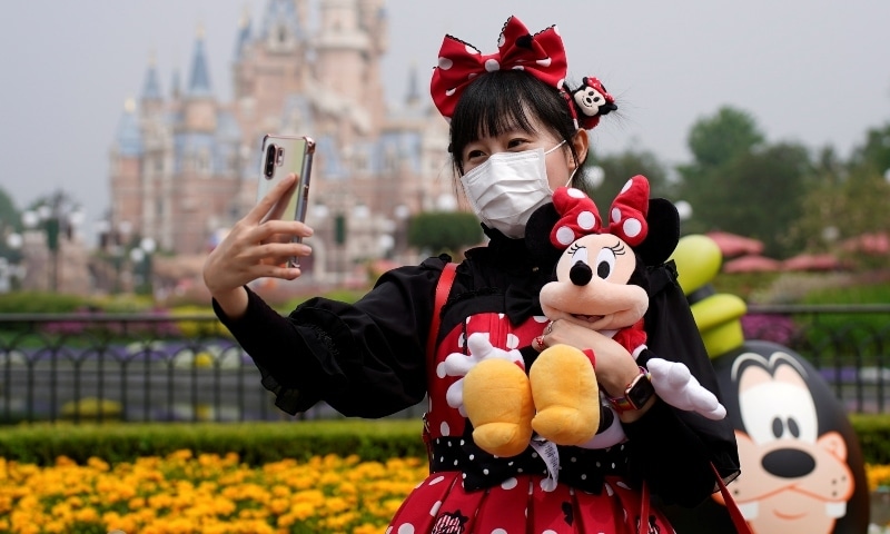 A visitor dressed as a Disney character takes a selfie while wearing a protective face mask at Shanghai Disney Resort on May 11. — Reuters