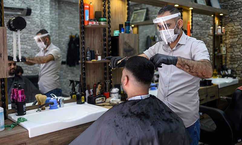 A barber wearing a protective mask cuts a man's hair in his shop on May 11 in Istanbul. — AFP