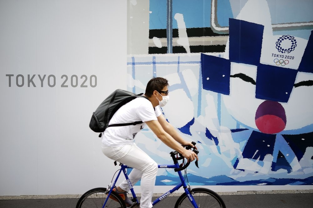 A man wearing a face mask to help curb the spread of the coronavirus rides a bicycle in front of an advertisement of Tokyo 2020 Olympic Games in Tokyo, Japan, May 12. — AP