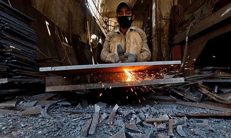 A worker cuts metal sheets with a gas blow torch at a workshop in Karachi on Tuesday. &mdash; Reuters