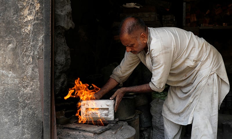 A worker, who makes auto parts, holds a mould near the fire at a workshop in Karachi. &mdash; Reuters