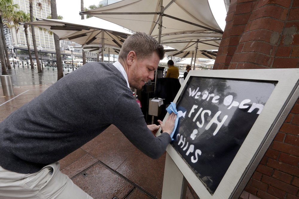 Alec Owes wipes a sign alerting customers that the Sydney Cove Oyster Bar is open as stage 1 of the lifting of Covid-19 restrictions begin in Sydney on May 15. — AP