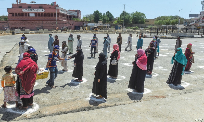 People stand in designated areas marked on the ground to maintain social distancing as they receive free food from volunteers in Karachi