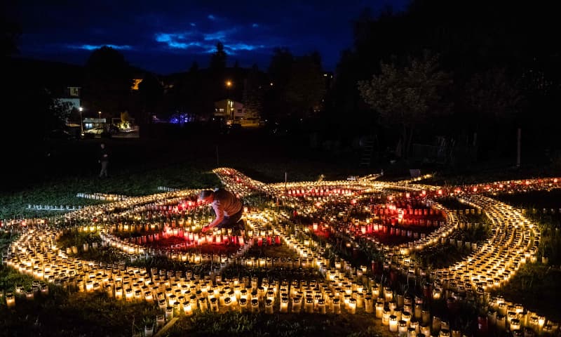 60-year-old Gertrud Schop lights candles arranged in the shape of a cross, with one candle dedicated to each of the more than 8,000 German Covid-19-related victims, in Zella-Mehlis, eastern Germany on May 19. &mdash; AFP