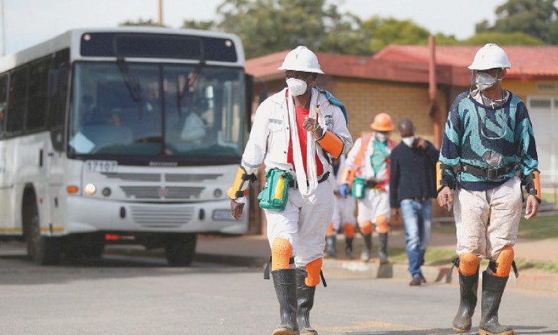 A FARMER’S son (left) raises his arms as he is surrounded by desert locusts while trying to chase them away from his crops in Katitika village, Kenya. Mine workers (right) wearing face masks arrive ahead of their shift at a mine of Sibanye-Stillwater company in Carletonville, South Africa.—Agencies