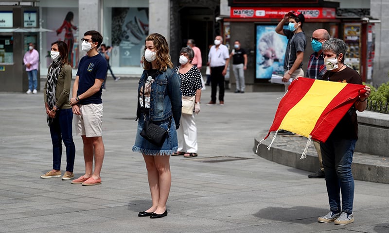 People wearing protective face masks stand during a daily minute of silence to commemorate victims of Covid-19 at Puerta del Sol square in Madrid, Spain, May 26. &mdash; Reuters