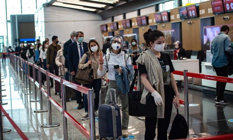 Travellers wearing protective face masks queue as an employee serves a passenger at the Istanbul Airport on June 1. &mdash; AFP