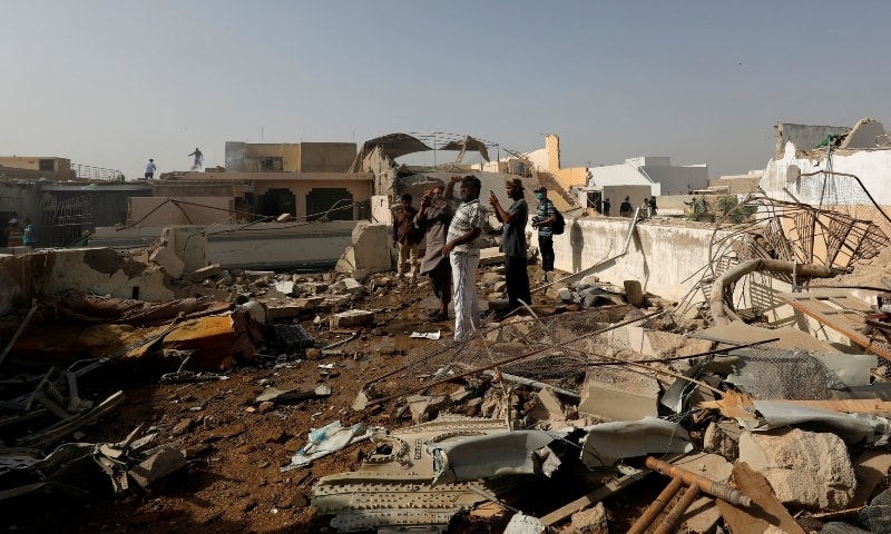 In this file photo, people stand on a roof of a house amidst debris of a passenger plane, crashed in a residential area near an airport in Karachi on May 22.  &mdash; Reuters